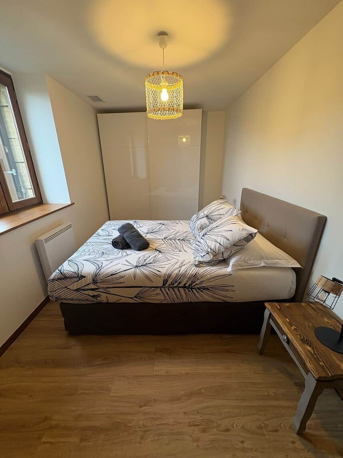 A bedroom with a bed, a hanging light fixture, a window, and a wooden bench.