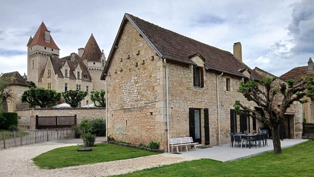 A stone building with a sloped roof, a paved driveway, and a grassy area with a bench and outdoor seating. - Gîte des Milandes * Vue imprenable sur le Château (Castelnaud-la-Chapelle)