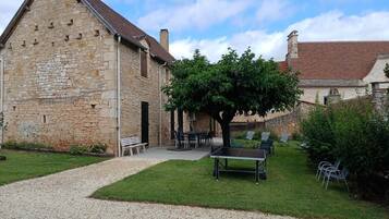 A stone building with a gravel path, outdoor seating, and a tree.