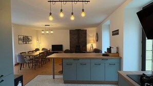 A modern kitchen with a central island, a dining area with a long table, and a TV in the background. - Gîte des Milandes * Vue imprenable sur le Château (Castelnaud-la-Chapelle)