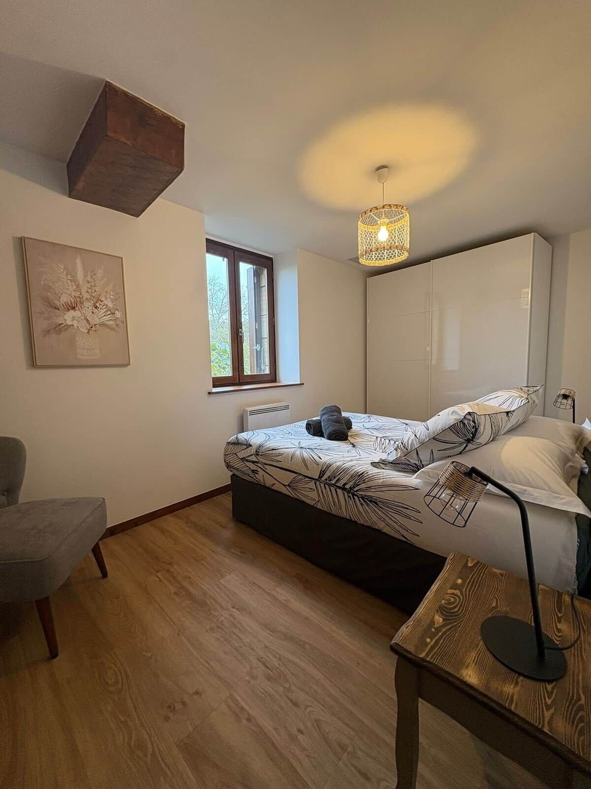 Une chambre à coucher comprenant un lit, une chaise, un bureau, un luminaire suspendu et une fenêtre.
