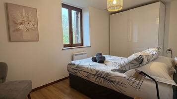 Une chambre à coucher comprenant un lit, une chaise, un bureau, un luminaire suspendu et une fenêtre.