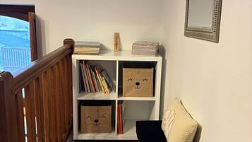 Een trap met een houten leuning, een witte boekenkast met boeken en decoratieve objecten, een zwarte stoel met kussen, en een spiegel aan de muur.