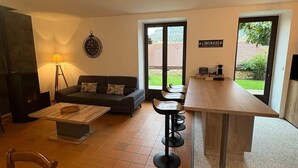 A living room with a sofa, a coffee table, a TV, a fireplace, and a bar area with stools. - Gîte des Milandes * Vue imprenable sur le Château (Castelnaud-la-Chapelle)