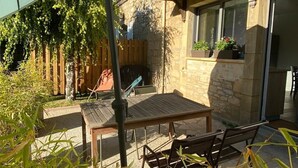 En terrasse med et bord og stole, et træhegn og en bygning af sten med et vindue.
