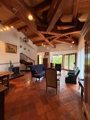 Un salón amplio con techo alto, vigas de madera, chimenea y un ventanal con vistas al exterior.
