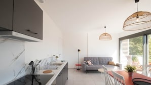 A modern kitchen with a black stove, white cabinets, and a dining area with a red table and white chairs. - Parenthèse Grand Air* Centre historique* parking lot (Sarlat-la-Canéda)