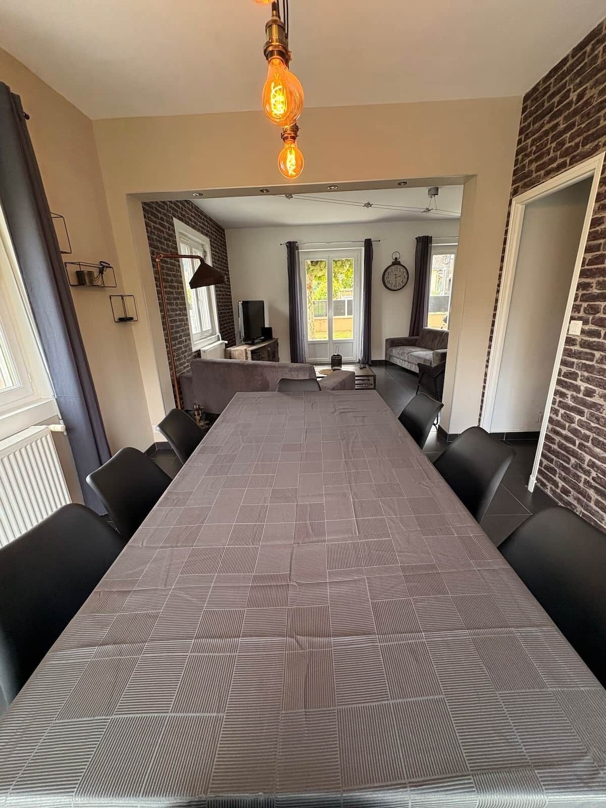 Una sala da pranzo moderna con un tavolo lungo, sedie nere, una parete decorata con mattoni e un lampadario.
