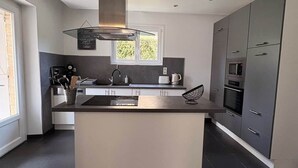 A modern kitchen with a central island, built-in appliances, and a window providing natural light. - Maison spacieuse* Jacuzzi* Proche cœur historique (Sarlat-la-Canéda)