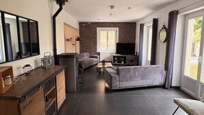 A modern living room with a sofa, a TV, and a kitchen area with a wooden cabinet. - Maison spacieuse* Jacuzzi* Proche cœur historique (Sarlat-la-Canéda)