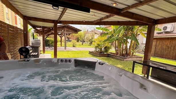 A hot tub under a covered patio with a view of a backyard and a barbecue grill. - Maison spacieuse* Jacuzzi* Proche cœur historique (Sarlat-la-Canéda)