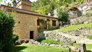 A stone building with a tiled roof, a small entrance, and a stone wall. - Nature and Charm*Pool*Beynac (Beynac-et-Cazenac)