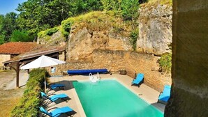 A swimming pool with lounge chairs, a stone wall, and a wooden pergola with an umbrella. - Nature and Charm*Pool*Beynac (Beynac-et-Cazenac)