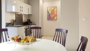 Uma cozinha moderna com armários brancos, uma mesa de jantar com cadeiras e um quadro abstrato colorido na parede.