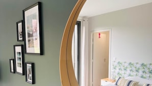 Quarto de hotel com uma cama, um espelho redondo, quadros nas paredes e uma pequena planta.