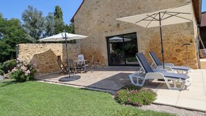 Ein Steinhaus mit einer Terrasse, die Gartenmöbel und Sonnenschirme bietet.