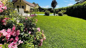 Ein Steinhaus mit gepflegter Rasenfläche und rosa Blüten im Vordergrund.