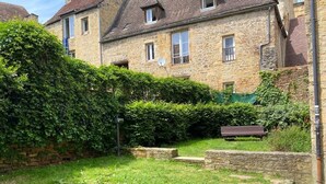 Un edificio de piedra con un patio cubierto de césped, una banca y un muro de piedra.