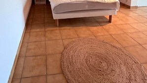 Quarto com uma cama, duas mesas de cabeceira, um tapete tecido e uma janela.