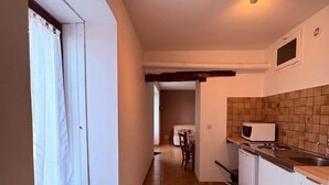 Uma cozinha pequena com piso ladrilhado, armários brancos, micro-ondas e pia.