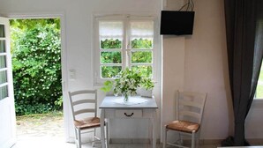 A room with a white table, two chairs, a TV on the wall, and a window with a view of greenery. - Villa 10 pers*Piscine*Daglan (Daglan)