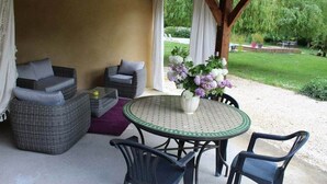 A covered patio area with wicker furniture, a round table with chairs, and a vase of flowers. - Villa 10 pers*Piscine*Daglan (Daglan)