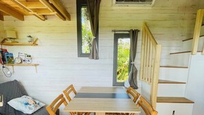 Ein Holzinnenraum mit Esstisch, Stühlen, einer Couch, einer Treppe und einem Fenster mit Vorhängen.