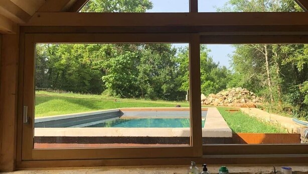 Une cuisine dotée d’une grande fenêtre donnant sur une piscine et un espace verdoyant.