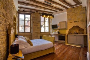 A bedroom with a wooden bed, stone walls, a stone fireplace, and a kitchen area. - "Betty C's apartments" Medieval studio (Sarlat-la-Canéda)