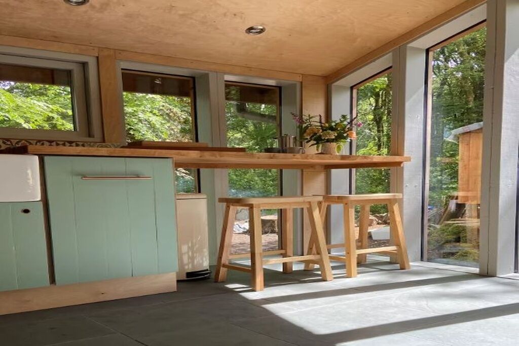Een moderne keuken met grote ramen, een houten aanrecht en een groene kast.