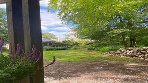 Un jardín con un sendero de grava, una estructura de madera y un montón de leña.