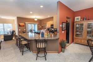 Una cocina con una isla central, taburetes de bar, armarios de madera y una zona de comedor con sillas.