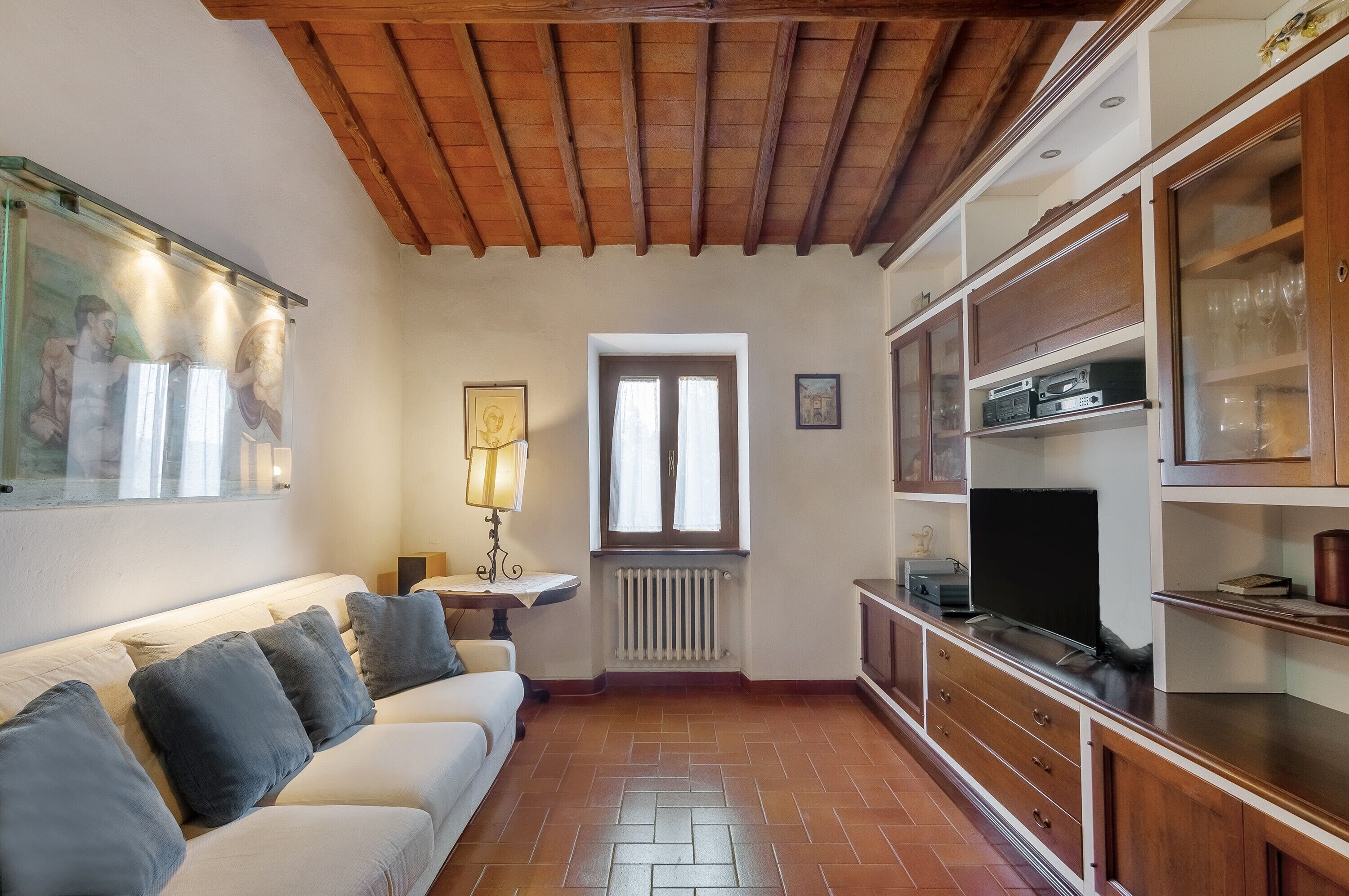 Un salon avec un plafond en bois, un canapé blanc, un radiateur, un téléviseur et des meubles en bois.