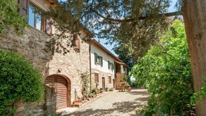 Un edificio in pietra con vialetto ghiaioso, porte in legno e persiane verdi.
