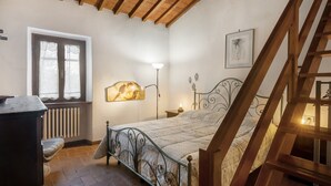 Una camera da letto con un letto, un termosifone, una finestra, una lampada, un quadro appeso al muro e una scala in legno.