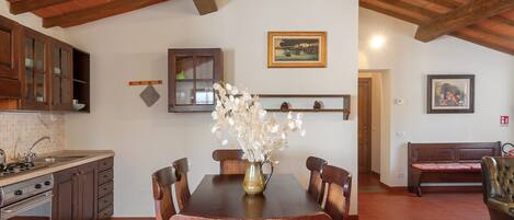 A kitchen with wooden cabinets, a dining table with chairs, a vase with flowers, and a painting on the wall.