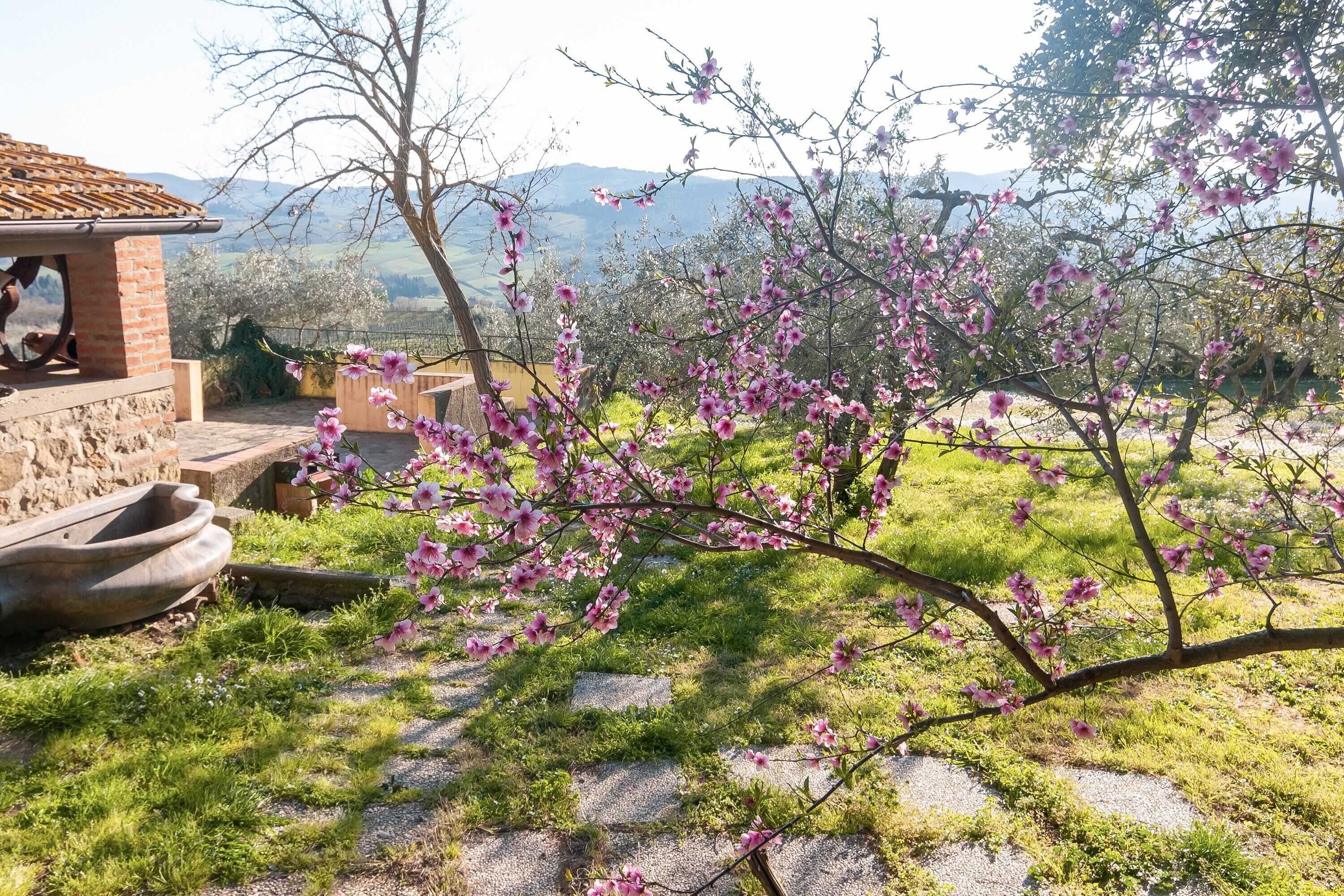 Un edificio in pietra con tetto in tegole, un giardino fiorito di fiori rosa e un panorama montuoso sullo sfondo.
