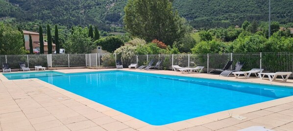 Una piscina rectangular con una valla blanca y sillas de descanso.