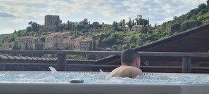 A person in a hot tub with a view of a historic town and a castle in the background. - Two-bedroom Apartment Montbrun-les-Bains (Special Rates for Spa Guests) (Montbrun-les-Bains)