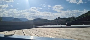 Terraza de madera con jacuzzi y vistas a montañas y una estructura que parece un castillo.