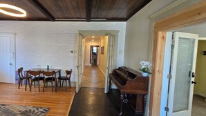 Ein Zimmer mit Holzboden, einem Esstisch mit Stühlen, einem Klavier und einer Tür zu einem anderen Raum.