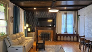 Ein Wohnzimmer mit Sofa, Kamin, Fernseher und Essbereich mit Stühlen.