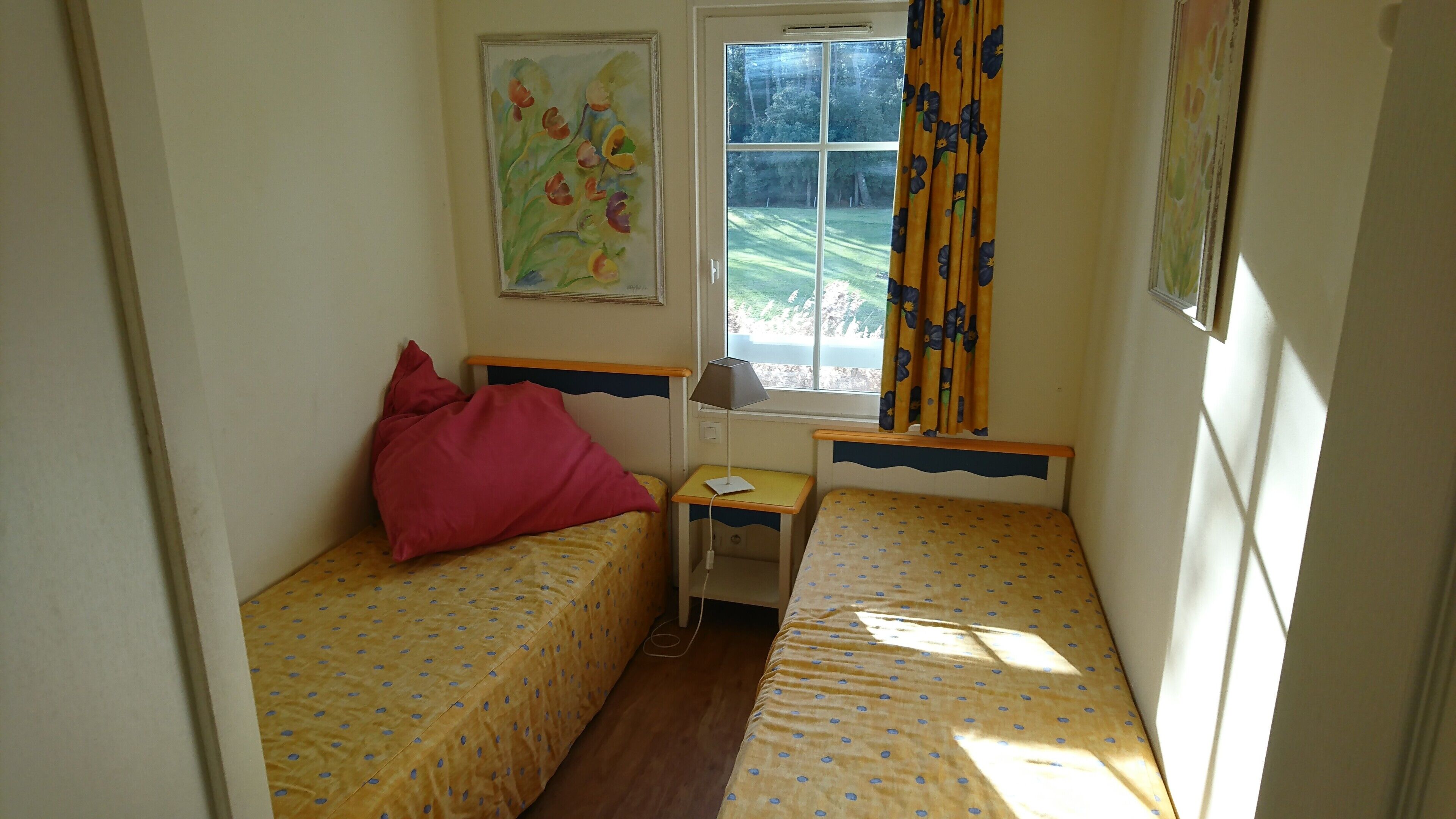 A small room with two single beds, a nightstand, a lamp, and a window with curtains.