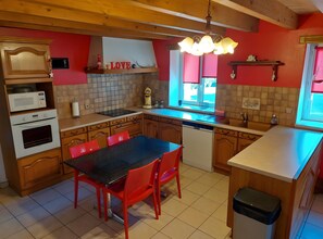 Keittiössä on puiset kaapit, musta työtaso, punaisilla tuoleilla varustettu ruokapöytä, mikroaaltouuni, uuni, astianpesukone ja kattokruunu.