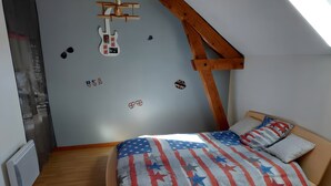 A bedroom with a sloped ceiling, a bed with a flag-themed bedspread, and wall decorations including a guitar and flags.