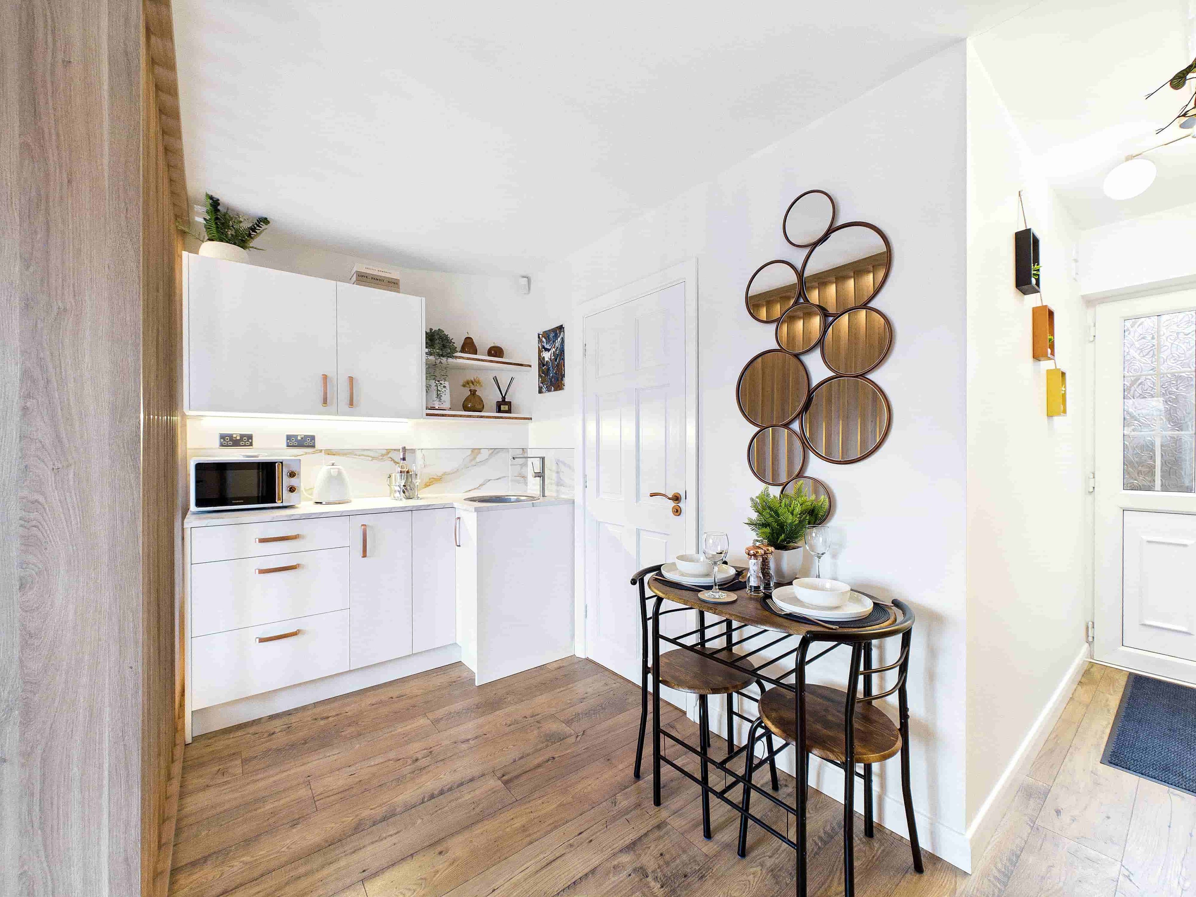A modern kitchen with white cabinets, a wooden floor, and a dining area with a round table and stools.