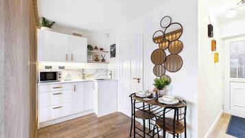 A modern kitchen with white cabinets, a wooden floor, and a dining area with a round table and stools.