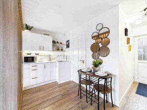 A modern kitchen with white cabinets, a wooden floor, and a dining area with a round table and stools.