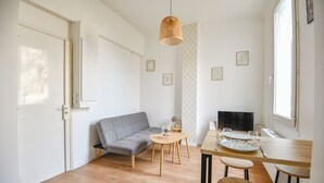 A modern living space with a grey sofa, a wooden dining table set for four, and a television. - Coeur Endoume - Bel appart 1 ch proche Vieux Port (Marseille)