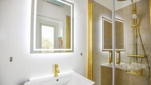A bathroom with a white sink, gold fixtures, and a glass shower enclosure. - Coeur Endoume - Bel appart 1 ch proche Vieux Port (Marseille)
